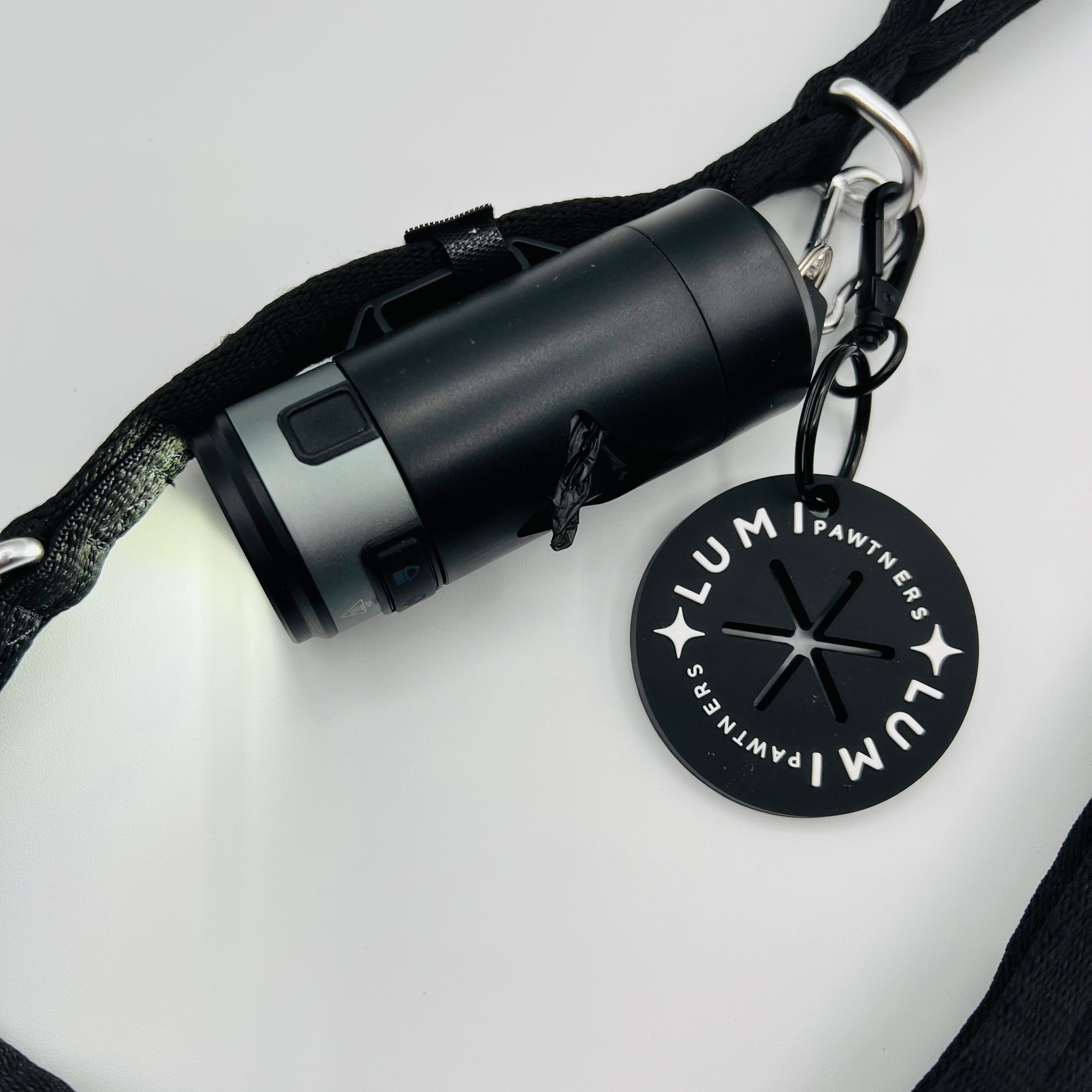Black waste bag holder with a Lumi poop loop on a white background